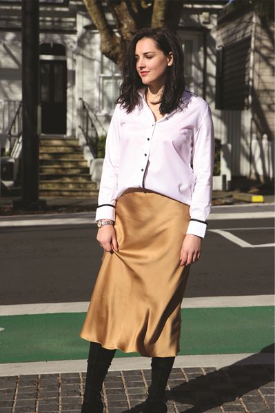 Elegant woman wearing a white blouse and gold satin skirt outdoors, showcasing stylish fashion for casual or professional settings.