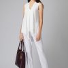 Elegant woman in white sleeveless blouse and trousers holding a designer handbag, showcasing stylish professional fashion for modern women.
