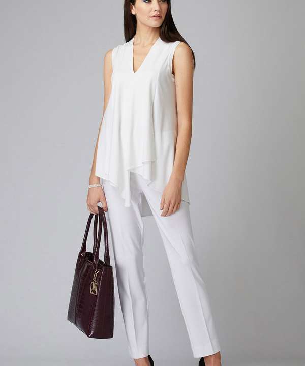Elegant woman in white sleeveless blouse and trousers holding a designer handbag, showcasing stylish professional fashion for modern women.