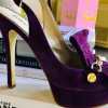 Luxurious purple velvet high-heeled shoe with bow detail and gold accents, perfect for elegant fashion statements and special occasions.
