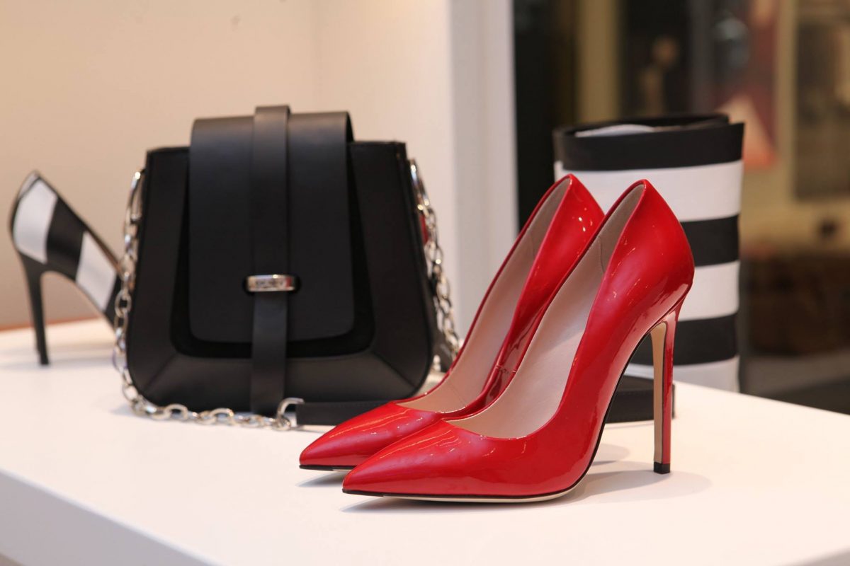 Stunning red high-heeled shoes with pointed toes and sleek design, paired with a chic black handbag featuring chain details, displayed on a white surface for luxury fashion shopping.