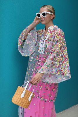 Vibrant floral embroidered sheer dress with oversized sleeves and pink skirt, stylish white sunglasses, and a wicker handbag, perfect for modern spring or summer fashion.