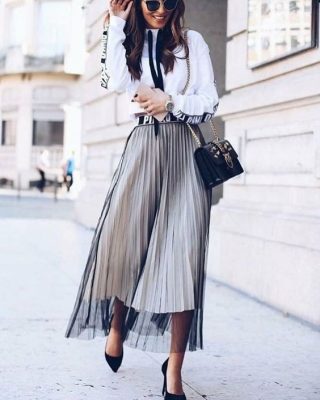 Stylish woman's street fashion featuring a pleated tulle midi skirt, white graphic hoodie, black handbag, and heels, perfect for chic urban outings and fashion-forward looks.