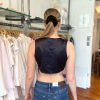 Elegant woman shopping for stylish clothing, wearing a black sleeveless top and blue jeans, inside a boutique store with neatly arranged garments, capturing a fashionable shopping experience.
