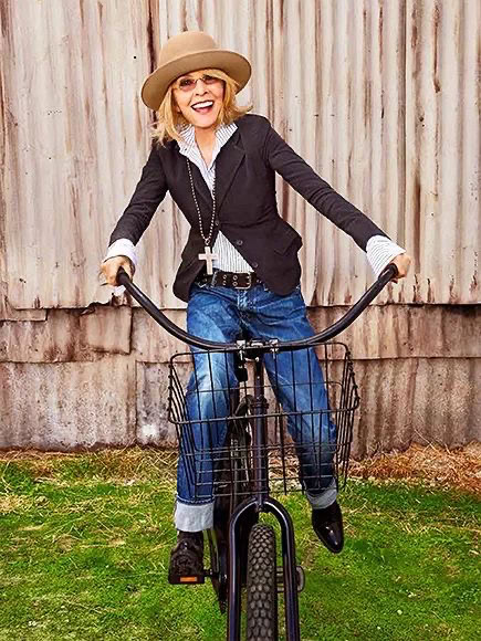 Vintage-inspired woman riding a black bicycle outdoors, dressed in casual chic with a hat, blazer, and jeans, showcasing a vibrant, fun, and bohemian style perfect for lifestyle and fashion photography.