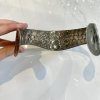 Hand holding a hammered metal bracelet with circular embossed design, showcasing handmade jewelry craftsmanship and artisanal metalworking.