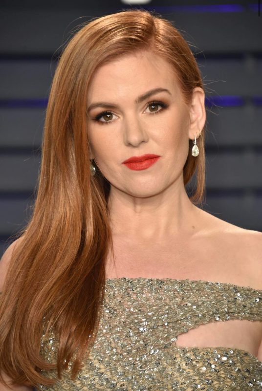 Elegant redhead woman with makeup, wearing diamond earrings and a gold embellished gown, posing at a formal event.