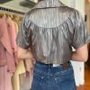 Button-up satin blouse with a shiny metallic finish and subtle striped pattern, paired with high-waisted blue jeans, showcased in a stylish boutique setting.