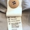 Button on beige fabric care label with instructions for dry cleaning, ironing, and moisture reduction, attached to a high-end garment by Katyamaker.