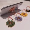 Colorful enamel floral hoop earrings displayed on a white surface with a smartphone nearby, showcasing trendy jewelry designs.