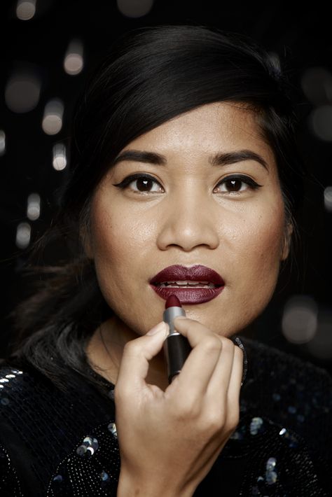 Vibrant woman applying deep burgundy lipstick, showcasing beauty, makeup artistry, and cosmetic products on katyamaker.com.