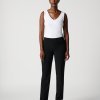 Elegant woman in black pants and white sleeveless top, standing confidently against a plain background, showcasing stylish business casual fashion with a modern, minimalist vibe.