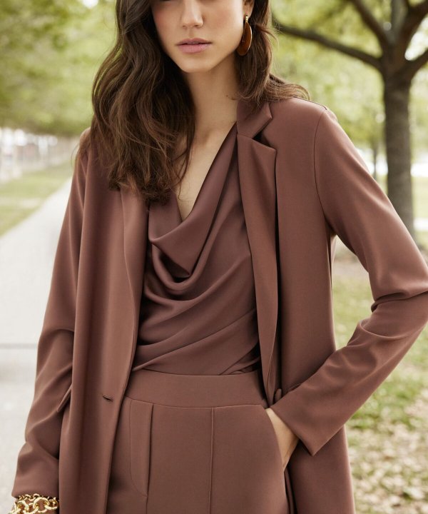 Elegant woman in brown tailored pantsuit and matching draped top, outdoor park setting, fashion photography, stylish professional attire, modern business look, katyamaker clothing collection.