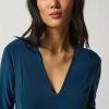 Elegant Asian woman in a teal V-neck dress posing against a plain background, showcasing stylish fashion and modern wardrobe essentials.