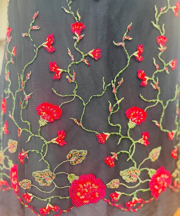 Luxurious black fabric featuring intricate red floral embroidery with green vine details, showcasing expert craftsmanship and delicate beadwork, perfect for elegant apparel and special occasions.