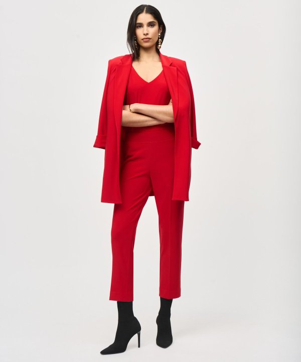 Professional woman in red business suit with blazer, pants, and high-heeled boots for fashion and business style, standing confidently against a white background, showcasing elegant and powerful corporate attire.