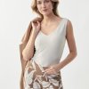 Elegant woman modeling stylish botanic print pants and a sophisticated sleeveless white top, holding a beige blazer over her shoulder, showcasing contemporary fashion and sustainable style.
