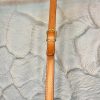 Handcrafted tan leather belt with gold buckle, featuring detailed stitching, displayed against a textured stone wall background for high-end fashion and accessory SEO.