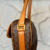 Leather handbag with monogram pattern, tan leather straps, and gold hardware on a textured white wall.