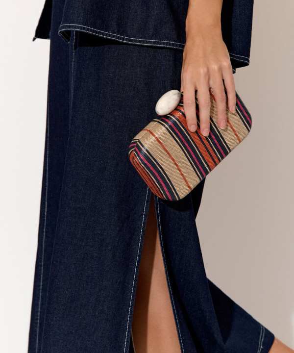 Striped fabric clutch bag with marble ring accessory held by a woman in denim outfit.