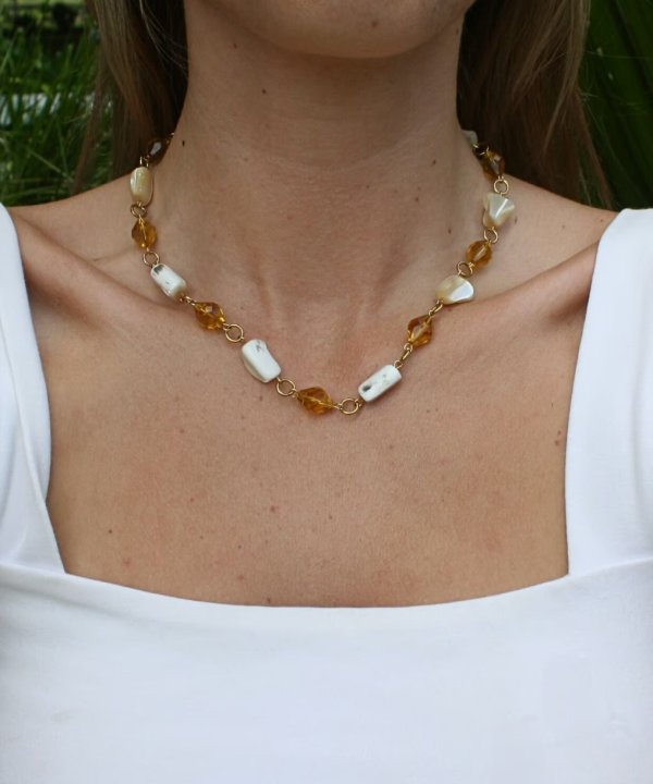 Golden amber and white baroque pearl necklace on a woman wearing a white top, close-up jewelry photo, handcrafted jewelry, natural stone necklace, elegant jewelry accessories.