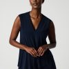 Navy sleeveless blouse with V-neck, stylish women's fashion, elegant top for professional or casual wear, paired with white pants, minimalist studio photography.