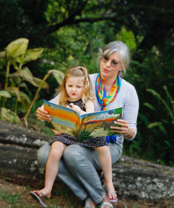 Reading book with grandmother and granddaughter outdoors in nature, promoting family bonding, literacy, and outdoor activities, sunny day, lush green background, children’s storybook, learning, nature exploration, bonding with family, outdoor reading, educational activities, storytime.