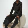 Elegant black fashion outfit featuring a stylish cowl neck top, wide-leg pants with tonal accents, and sleek pointed high-heel boots, styled in a minimalist studio setting.